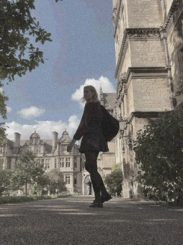 Saulutė Monika senojo universiteto kieme tarp akmeninių pastatų, atsigręžusi atgal